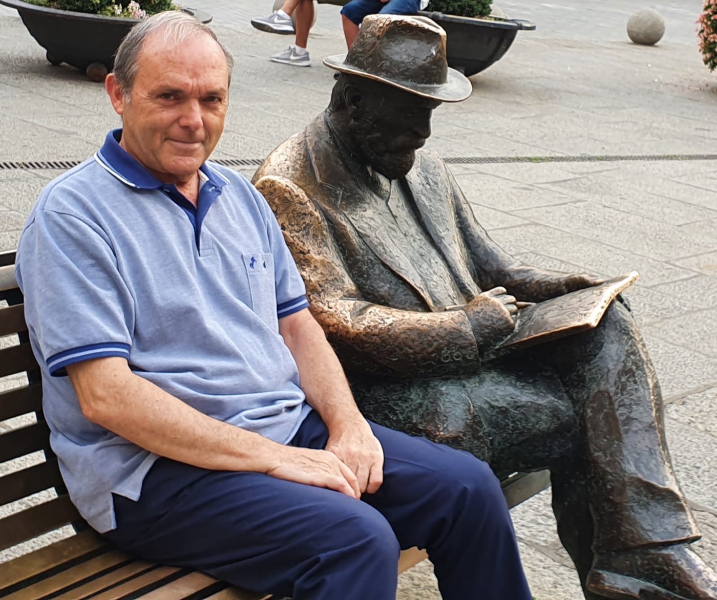 José Manuel Almuzara sentado en un banco junto a una estatua de bronce de Antoni Gaudí, representado sentado y leyendo un libro