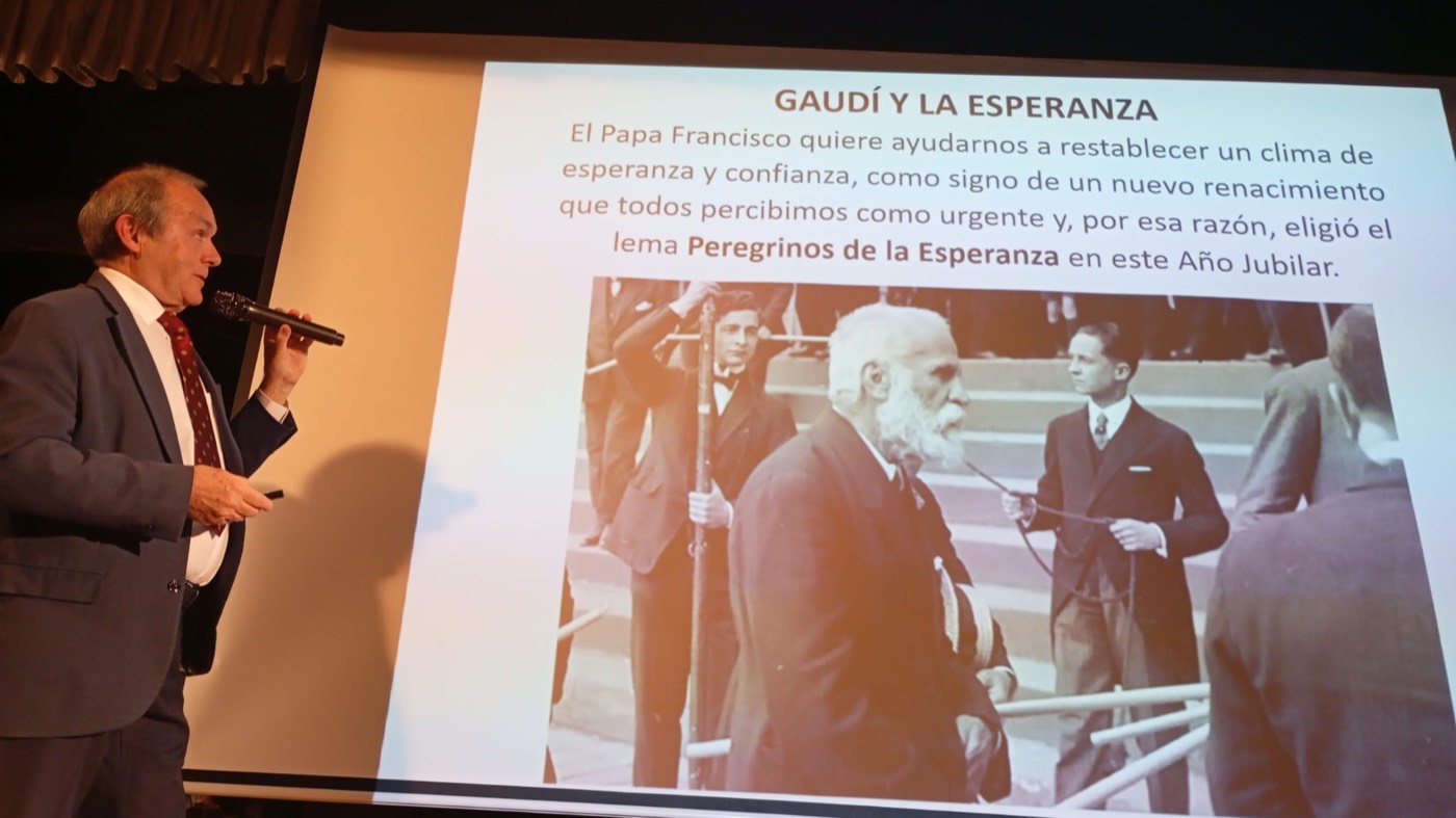 Un hombre con micrófono en la mano da una conferencia ante una pantalla con el título «Gaudí y la Esperanza» y una fotografía antigua de dos hombres.
