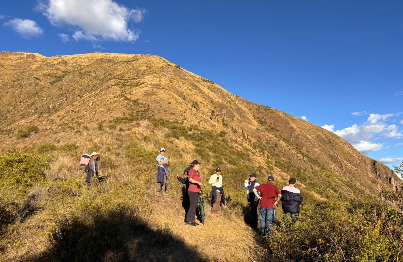 Grupo de personas caminando por una ladera de montaña árida bajo un cielo azul.