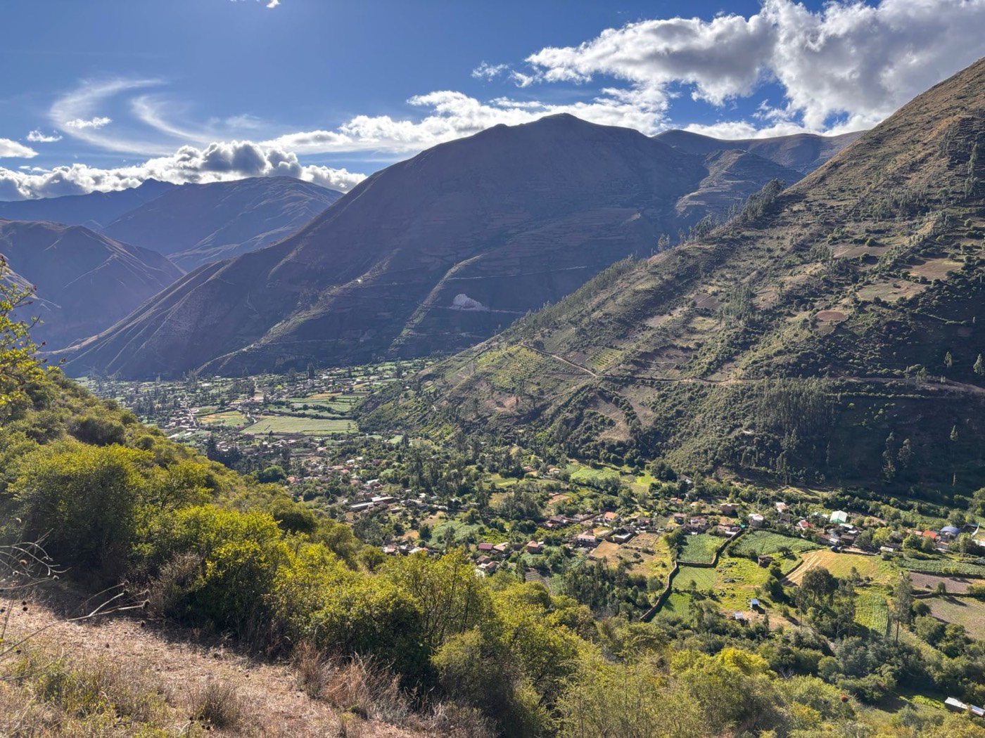 Vista panorámica de un valle andino verde entre montañas, con un pequeño pueblo al fondo.