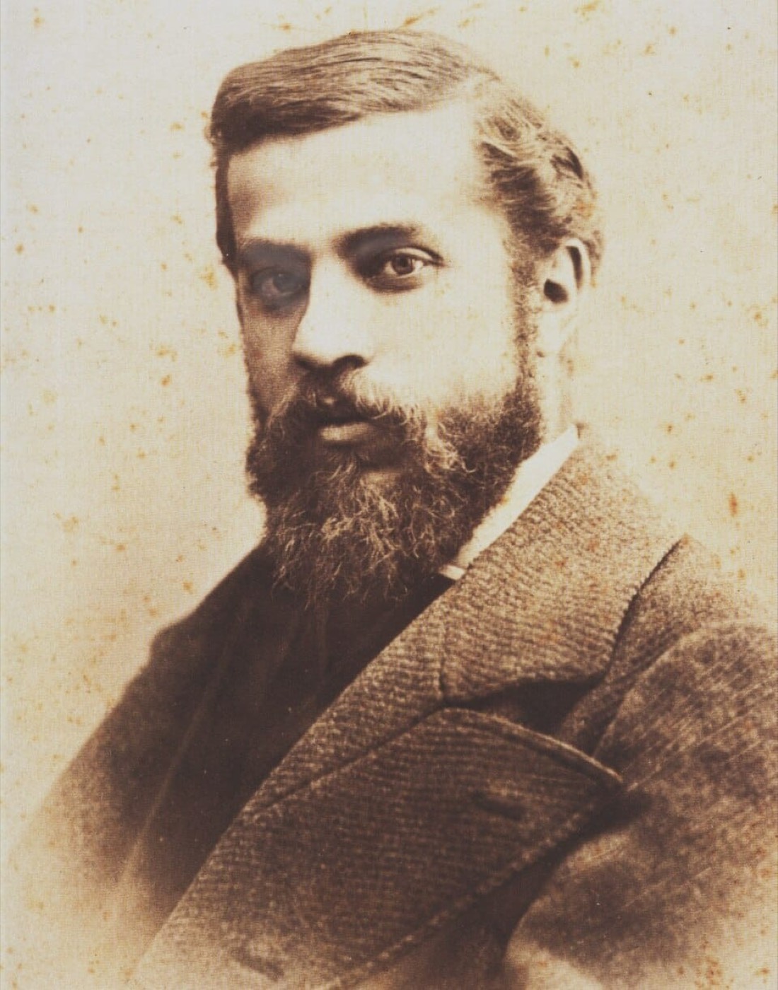 Retrato fotográfico antiguo en tono sepia de un hombre joven, con barba y bigote, vestido con abrigo de época.