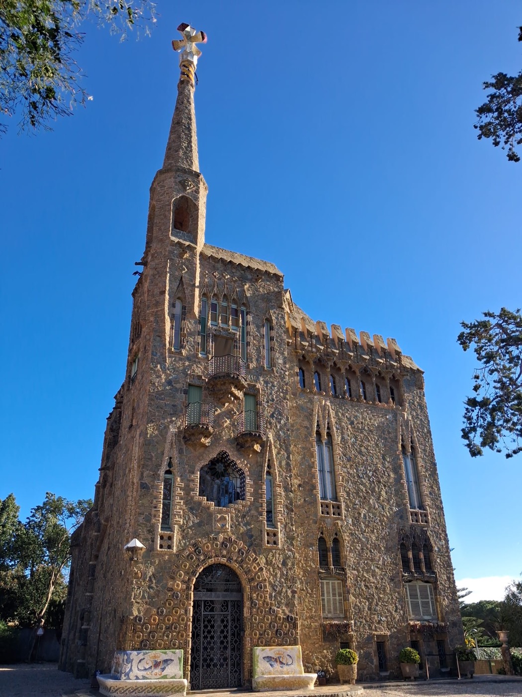 Fachada principal de la Torre Bellesguard en Barcelona, con su torre-mirador rematada por una cruz de cuatro brazos, bajo un cielo azul despejado.