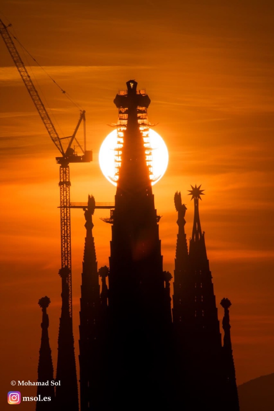 Silueta de las torres de la Sagrada Família al atardecer, con el sol poniéndose justo detrás de la cruz de la torre central.