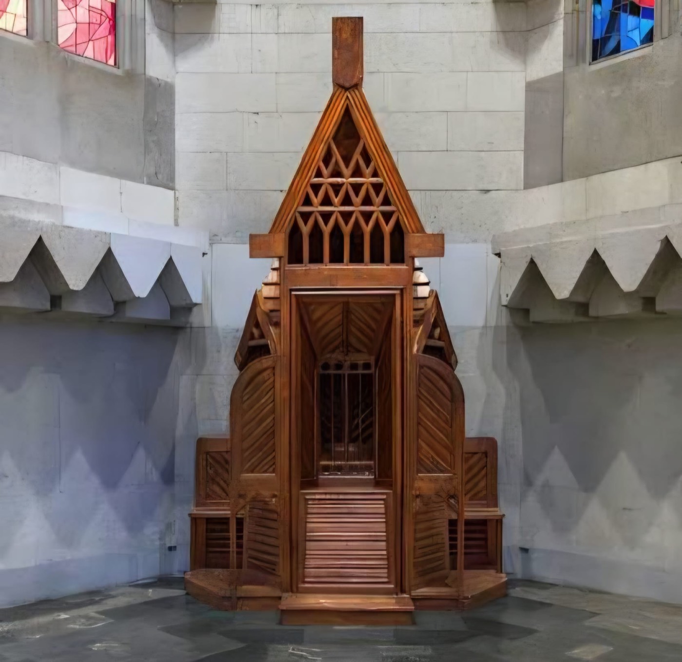 Confesionario de madera diseñado por Gaudí, de planta hexagonal con remate en forma de aguja, instalado bajo unas vidrieras de colores en el interior de la Sagrada Família.