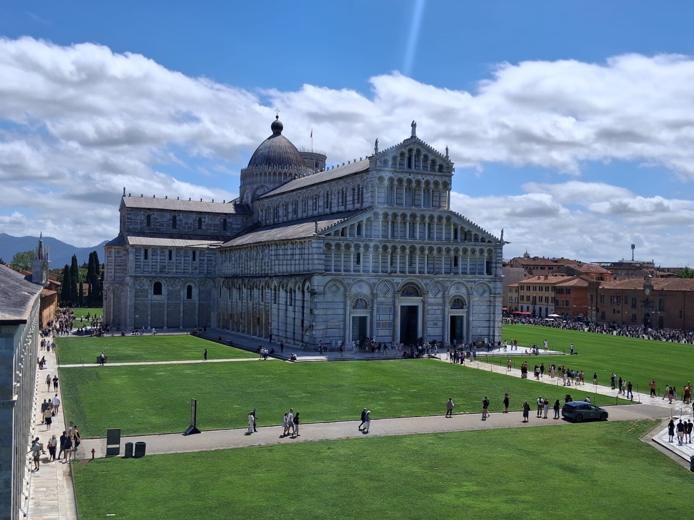 Fachada de la Catedral de Pisa vista desde el césped de la Piazza dei Miracoli, con turistas paseando.