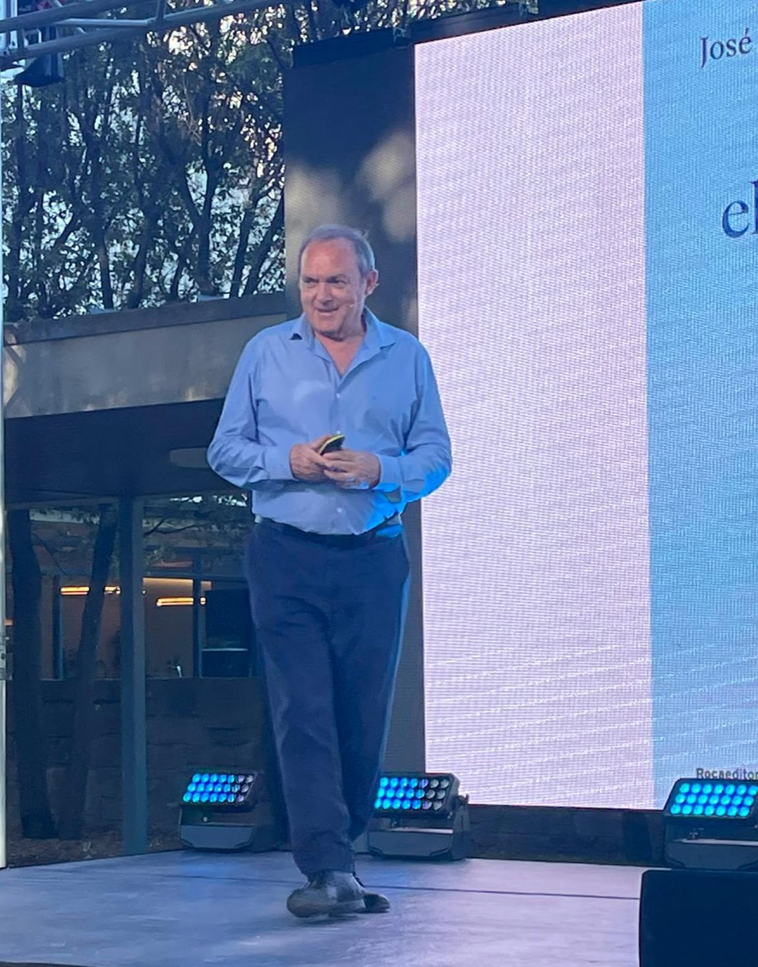 José Manuel Almuzara camina sobre un escenario al aire libre con un micrófono, ante una gran pantalla de proyección.