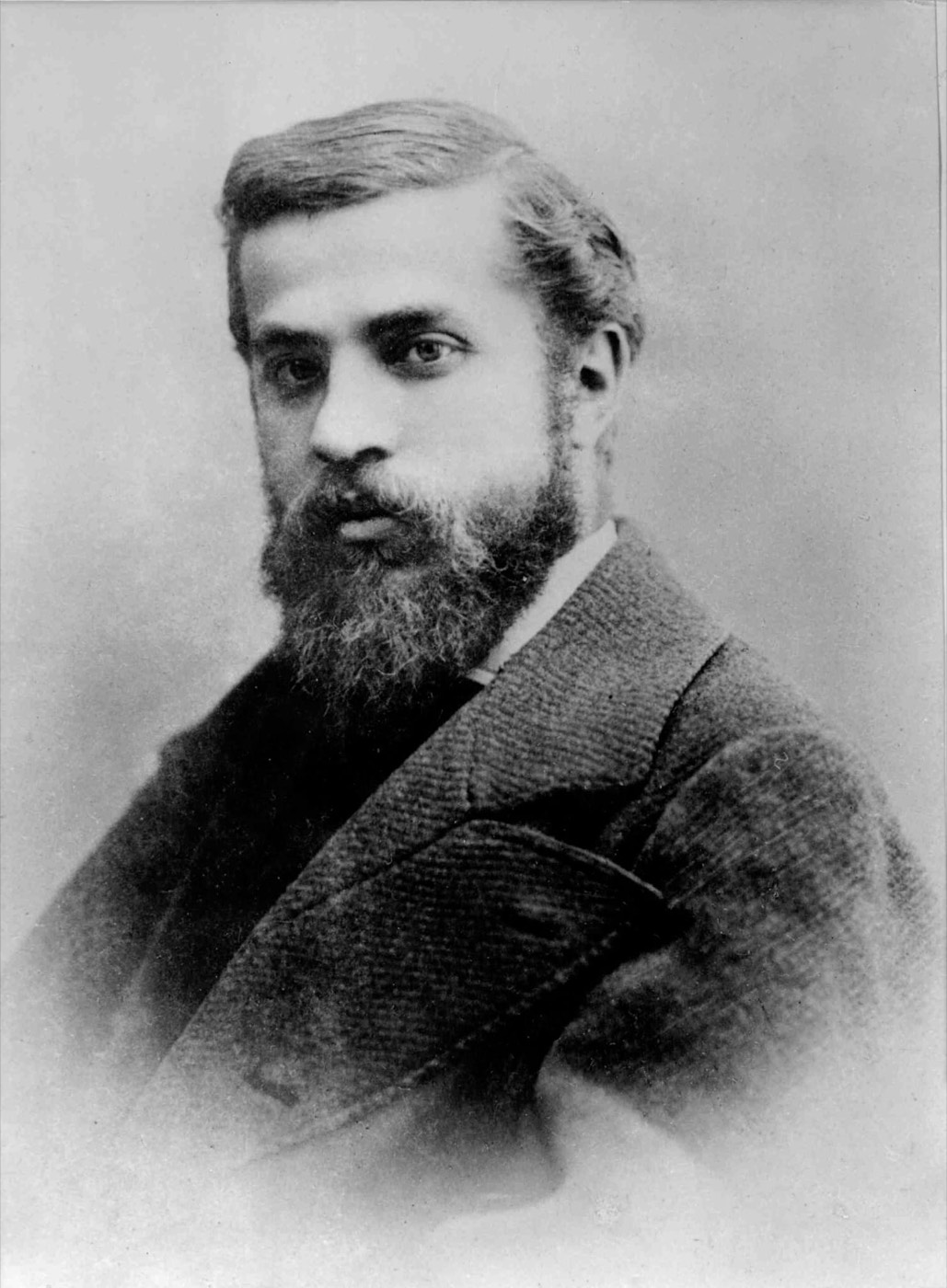 Retrato fotográfico histórico en blanco y negro de un joven Antoni Gaudí, con barba y traje de época.