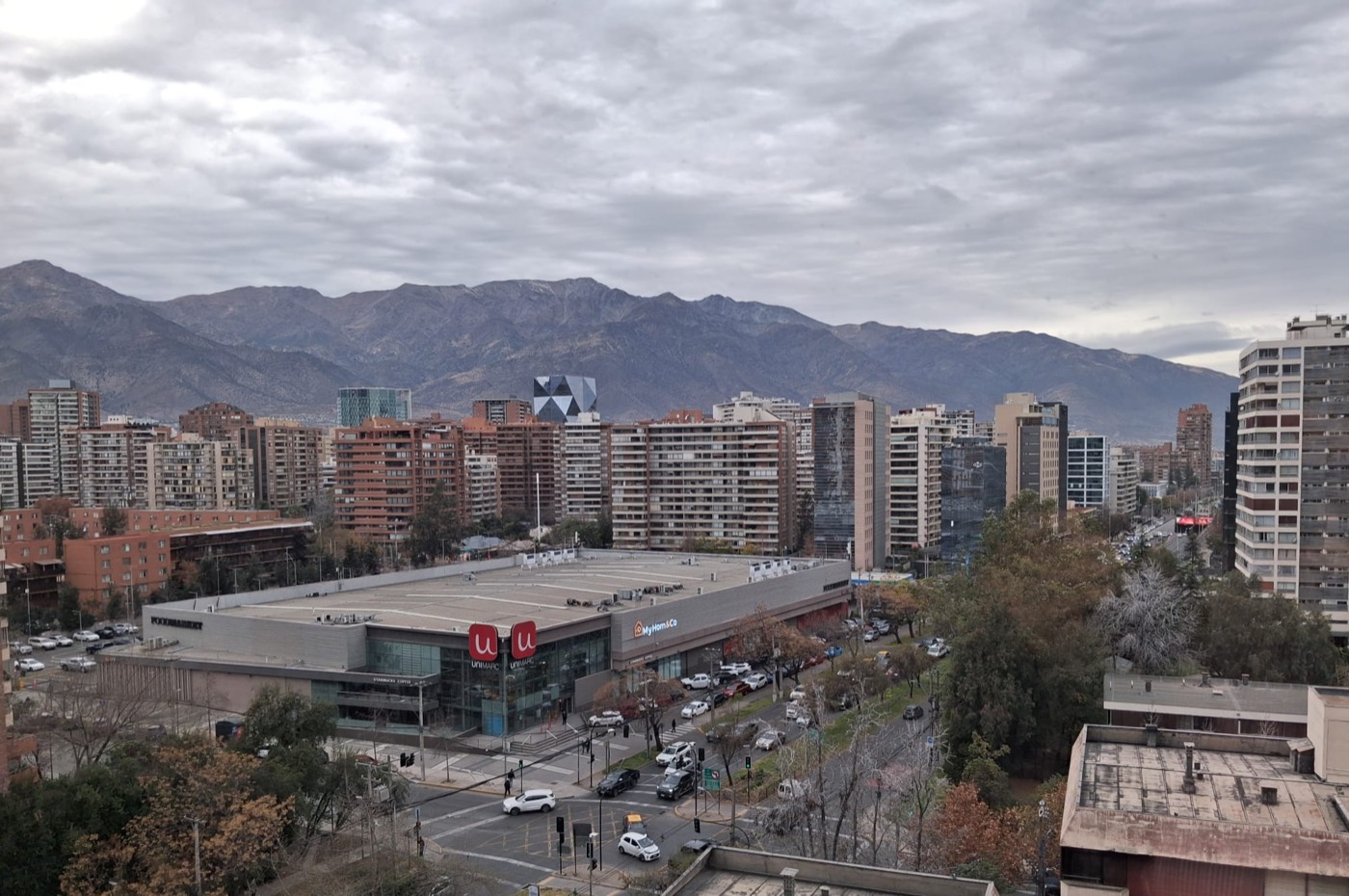 Vista de Santiago de Chile desde una ventana en un día nublado, con edificios y la cordillera de los Andes al fondo.