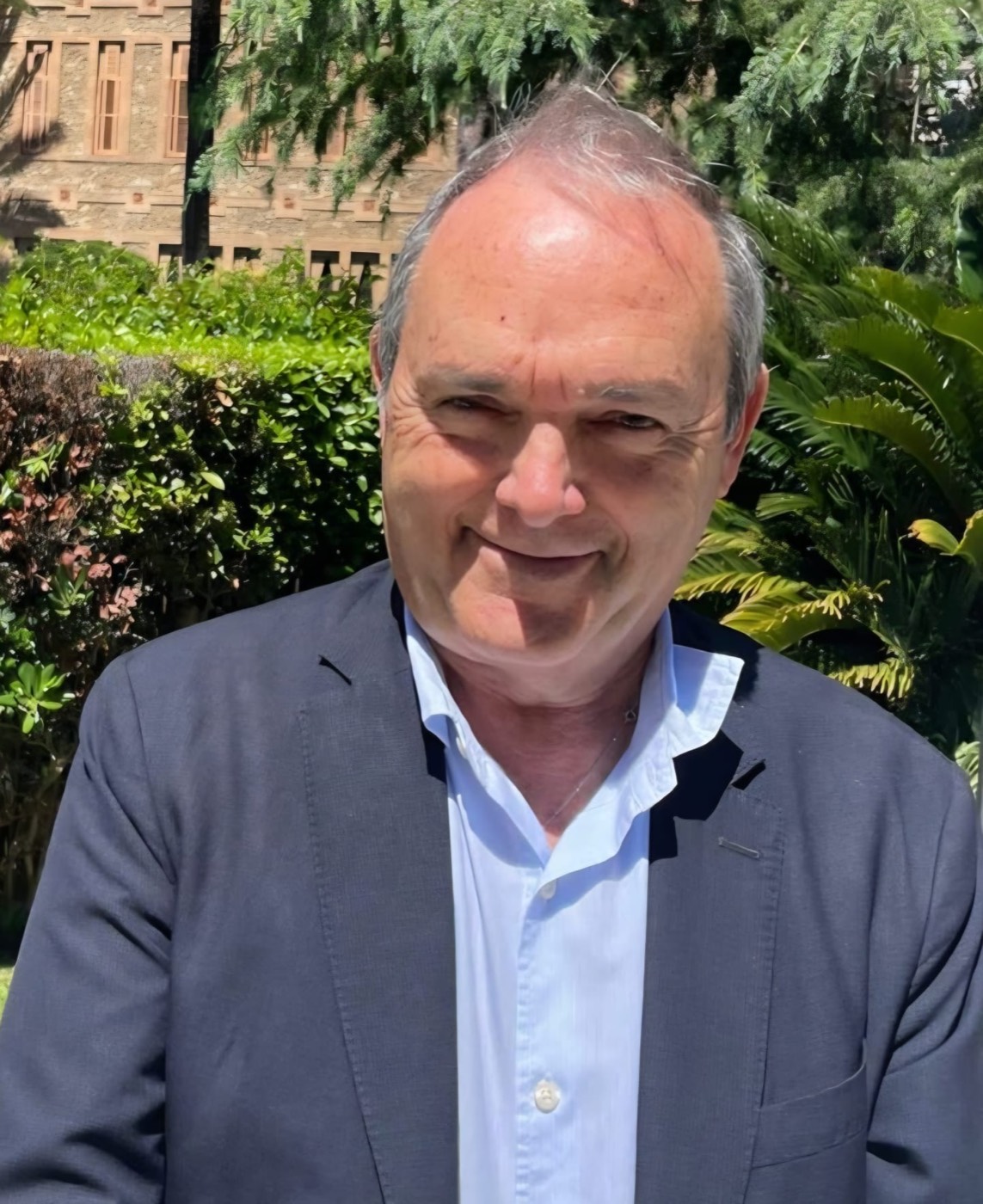 José Manuel Almuzara sonríe al aire libre, entre setos verdes, con un edificio desenfocado al fondo.
