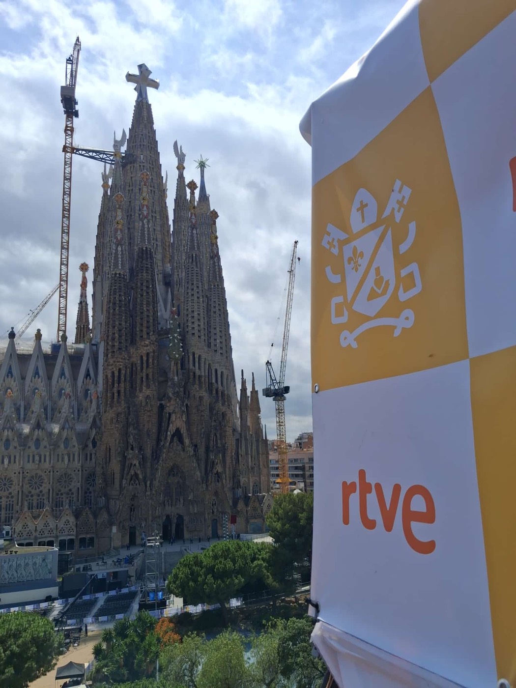 Vista de las torres de la Sagrada Família desde una azotea, junto a una lona con el logotipo de RTVE.