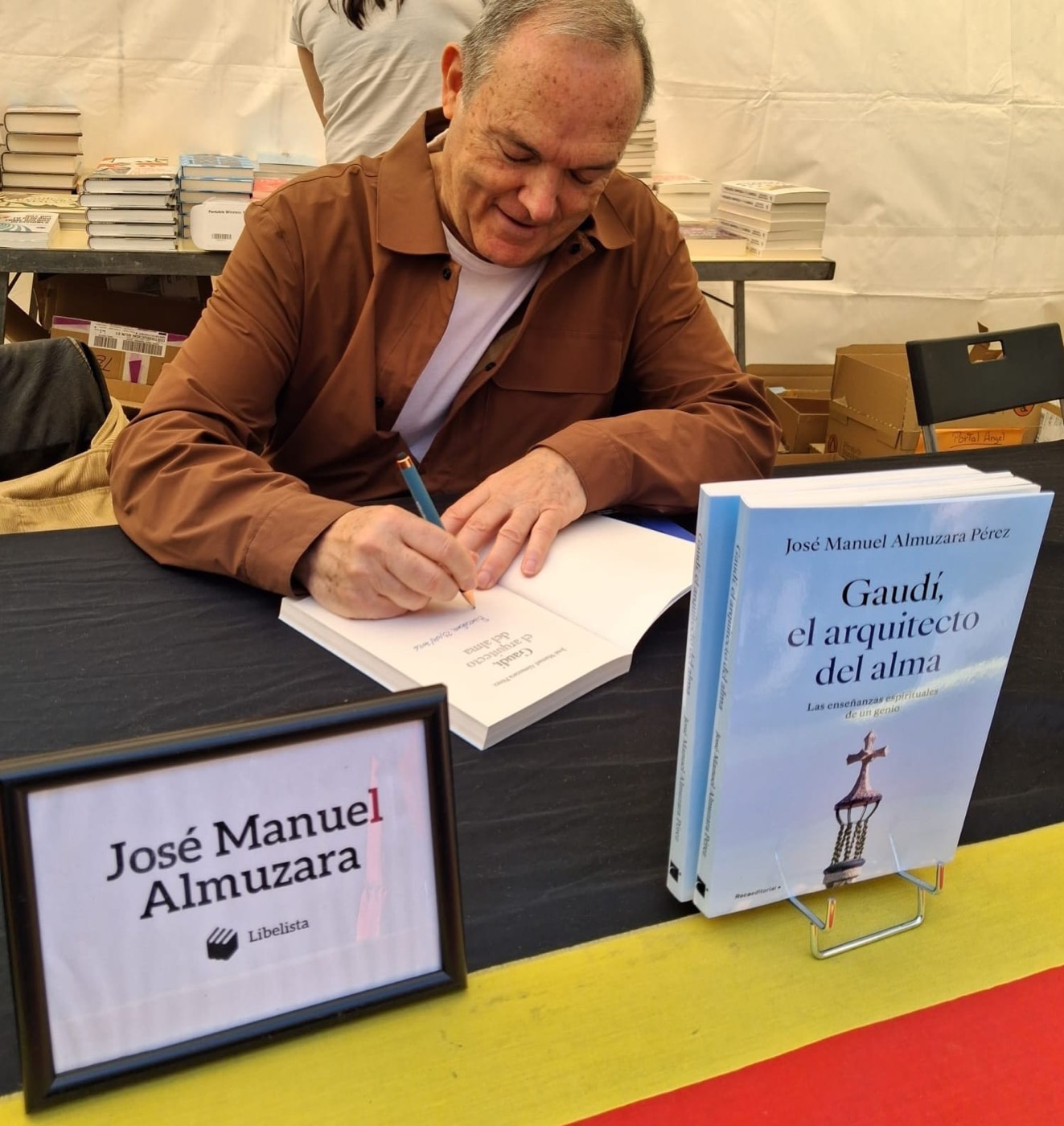 José Manuel Almuzara firma ejemplares de su libro 'Gaudí, el arquitecto del alma' en una mesa con un cartel con su nombre.